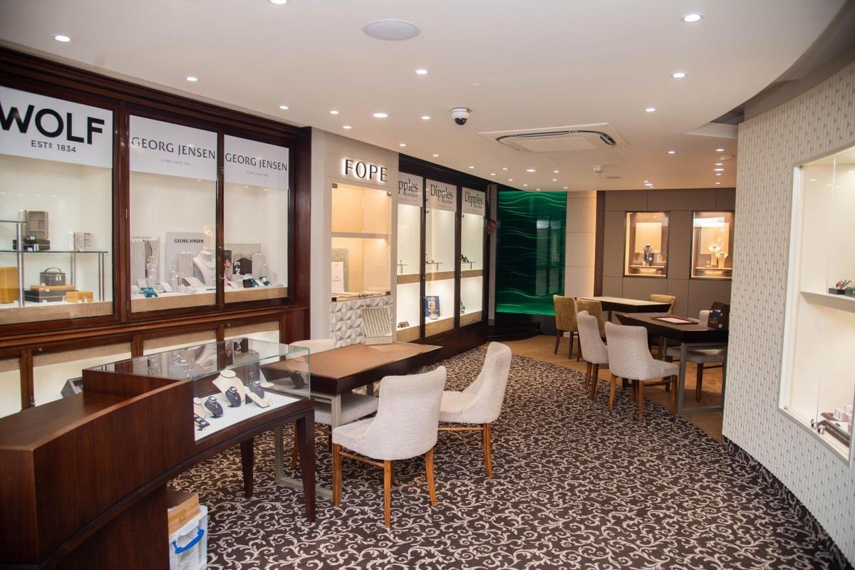 Interior of the Dipples Bury St Edmunds showroom with Georg Jensen, FOPE and Wolf cabinets, white consultation chairs and the green-lit jewellery vault at the rear